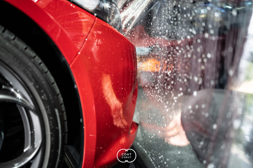 Water beading on the front quarter of a red car with fresh paint protection film